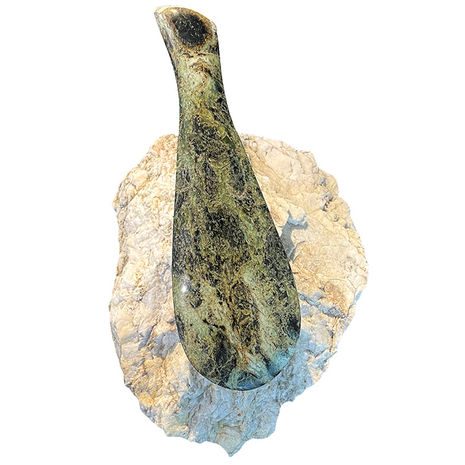 Beautifully carved NZ greenstone mere resting on a quartz rock.