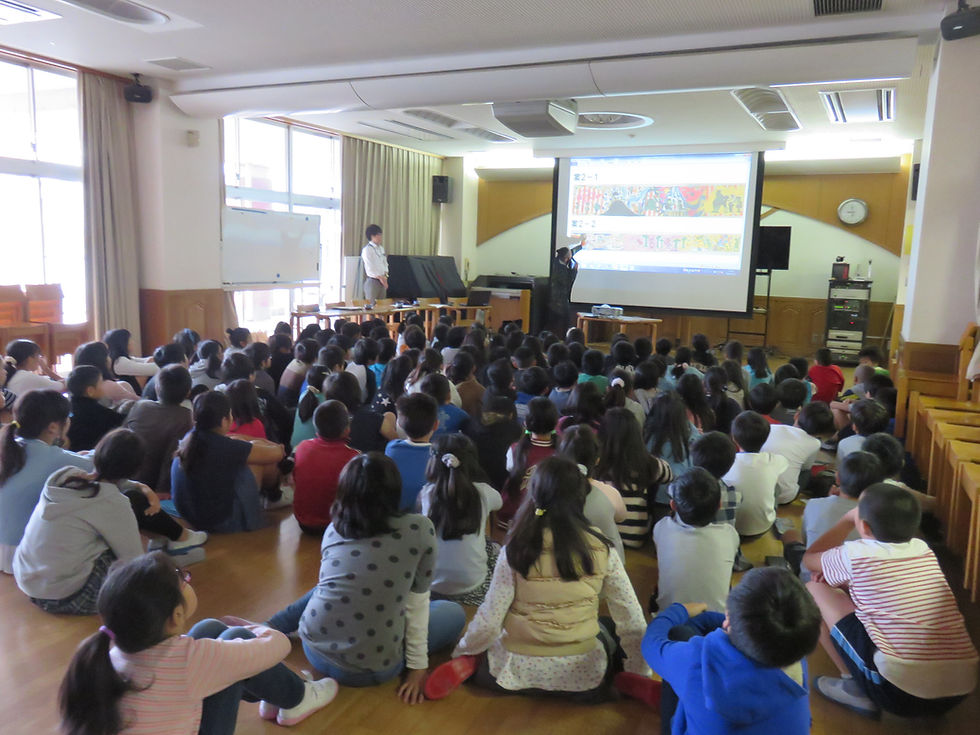 体育館でスクリーンを見る大勢の小学生