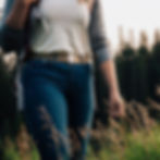 women walking in tall grass in blue jeans, a white t-shirt and a backpack, wearing a belt