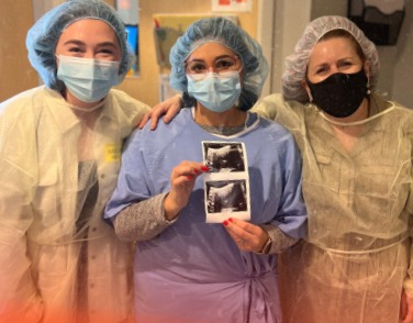 Three people in medical gowns holding a sonogram