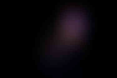 Carla Geneve performing onstage at QPAC Concert Hall, standing with an acoustic guitar under soft, warm lighting.