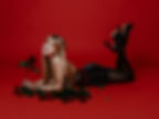 A young woman lying on her front eyes a beautiful red rose. She's in a black dress and huge high heels kicked up in. the air