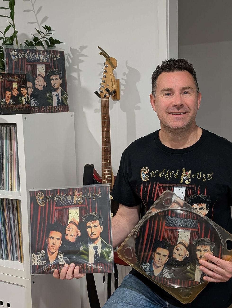 Matt Jones sits posing in front of a guitar and in possession of many copies of Crowded House's seminal sophomore album, Temple Of Low Men