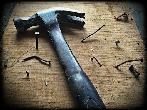 A hammer on a table surrounded by nails