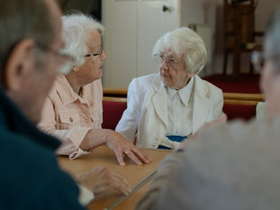 Personas mayores conversan sentadas alrededor de una mesa en un espacio comunitario.