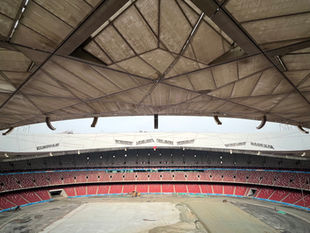 Amplia vista interior de un estadio vacío con graderías y estructuras en proceso de renovación.