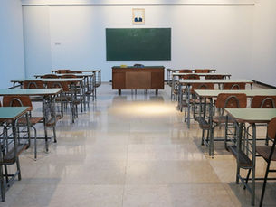 Imagen referencial de una sala de clases vacía con escritorios y pizarra.