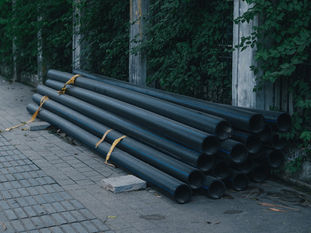 Tuberías negras para una obra de agua y saneamiento apiladas junto a un camino.
