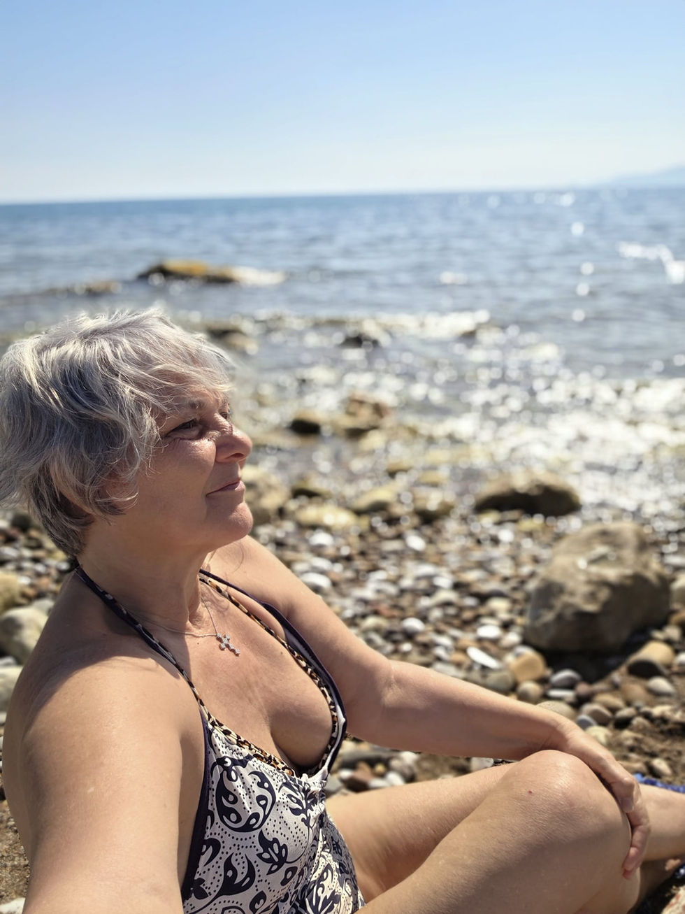 Donna matura seduta sul mare mentre riflette sul benessere e sull'accettazione della propria età