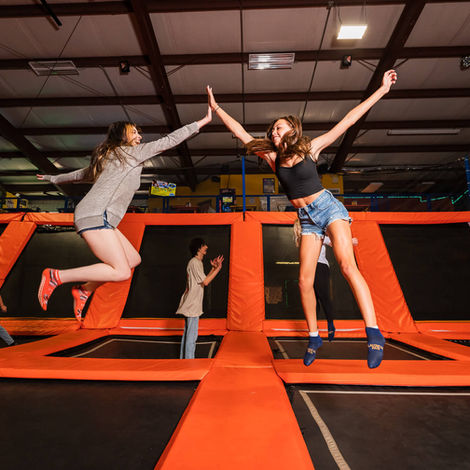 A photo of 2 teenage girls at Launch Pad trampoline park. They are jumping on trampolines, mid air giving each other a high five.