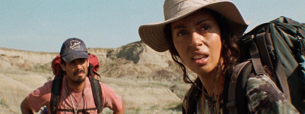 An image of actors Clark Backo as Lauren and Drew Ray Tanner as Ben in the movie Split Rock. In the image, they are standing in the Canadian Badlands, surrounded by rocky terrain, as they look straight ahead.