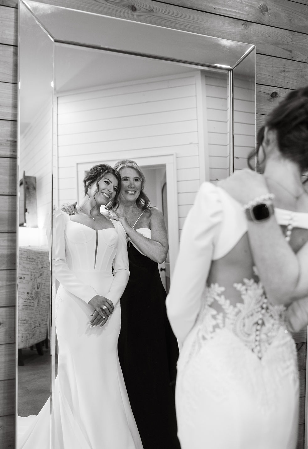 The bride and her mother smiling as they look in the mirror together. Black and white, happy mood.
