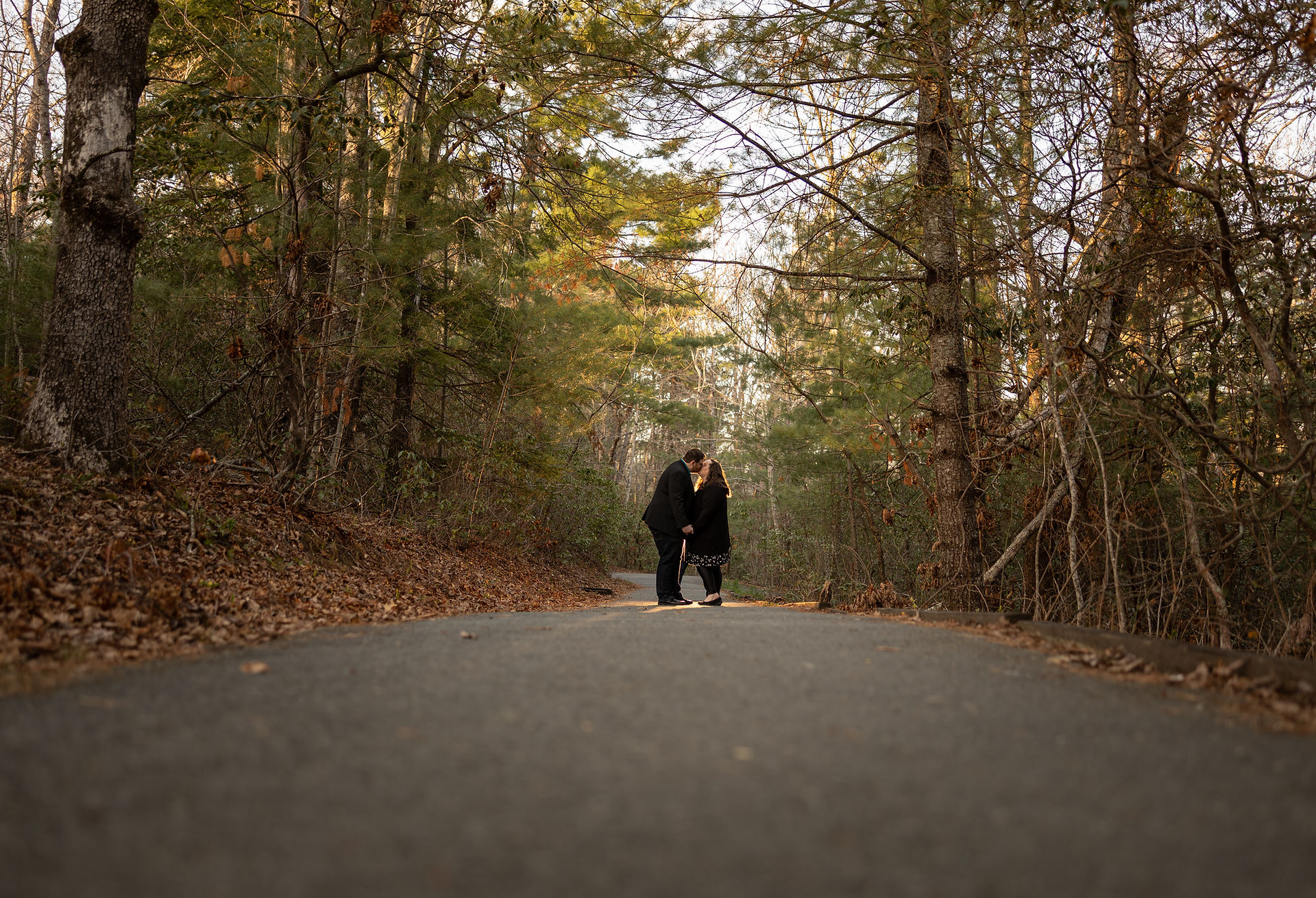 A couple kisses while on a nature path in the woods.
