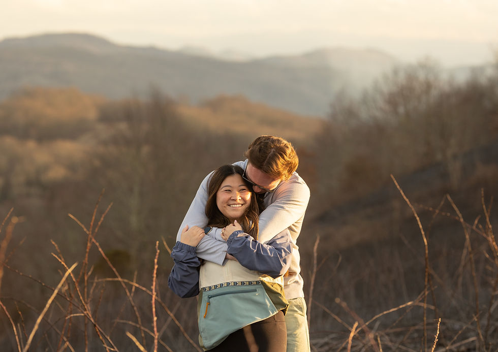 Couple embracing happily on a mountain trail, surrounded by dry branches and rolling hills in the warm, golden glow of sunset.