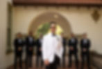 The groom smiling as he stands in front of the groomsmen.