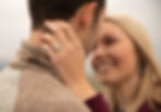 a woman's engagement ring in focus as she smiles in the background