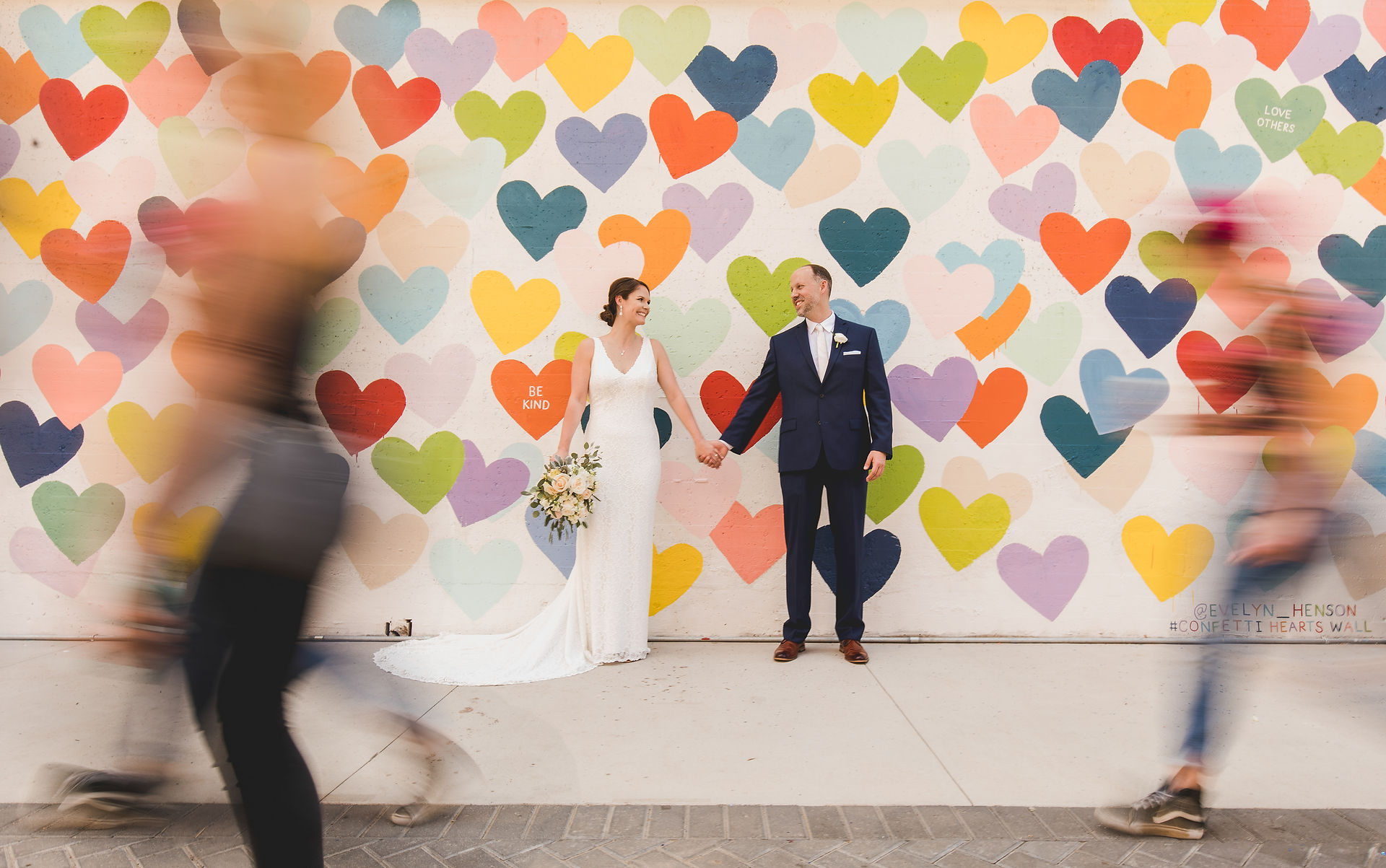 bride and groom holding hands in front of a heart wall 