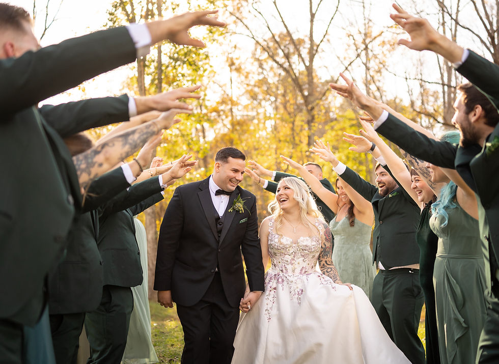Bride and groom walk joyfully hand-in-hand under an arch of raised hands outdoors, surrounded by cheering guests in green attire.