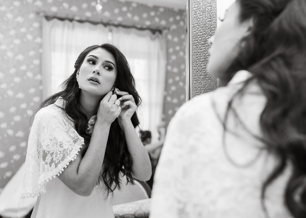 The bride looking at herself in the mirror as she puts her earrings on.