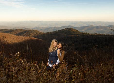 A woman smiles as her fiance hugs her from behind in the mountains. 