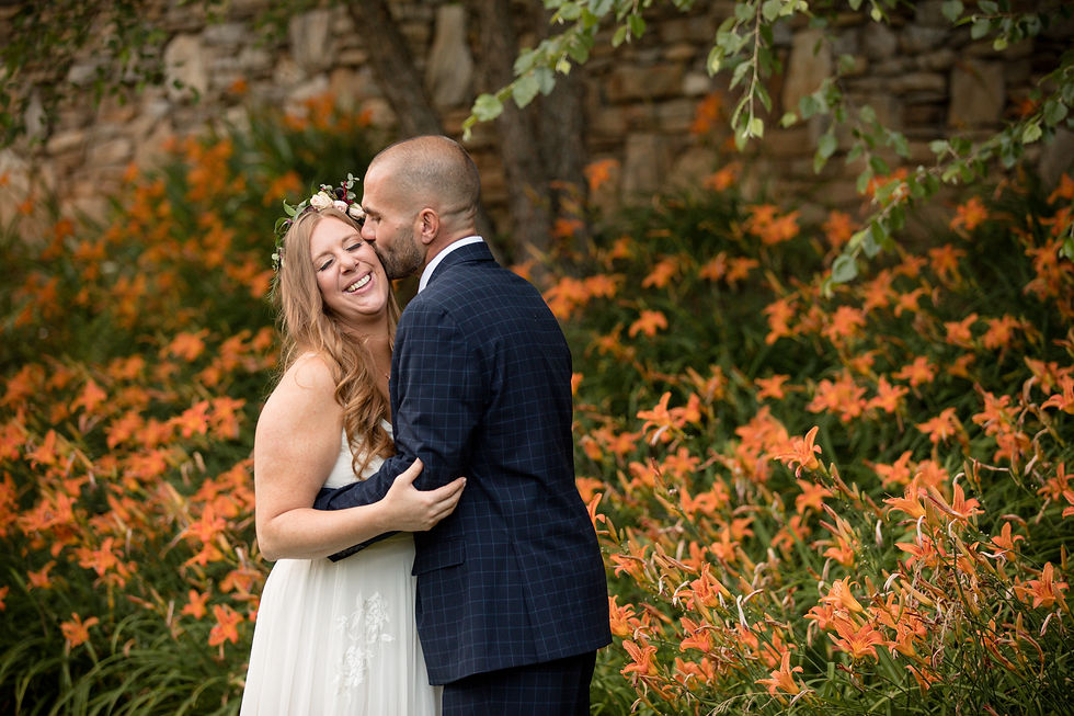 groom kissing bride's cheek in front of orange flowers