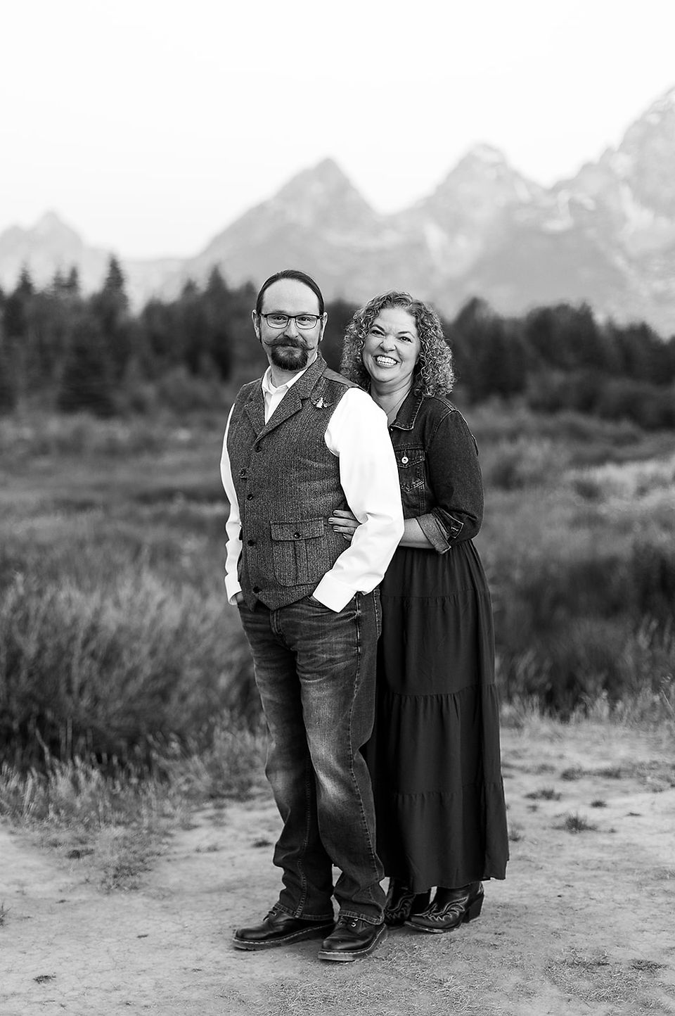 a couple smiling as she hugs her husband from behind 
