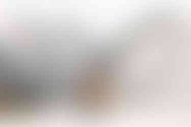 A bride and groom stand in the middle of a snow covered field with towering snow capped mountains in the background. The groom is wearing a cowboy hat and the bride is looking the opposite direction and holding her hat.