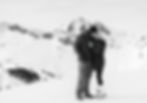 Couple kissing on a snowy mountain, wearing winter clothes. Background features snow-covered peaks, creating a romantic, serene mood.