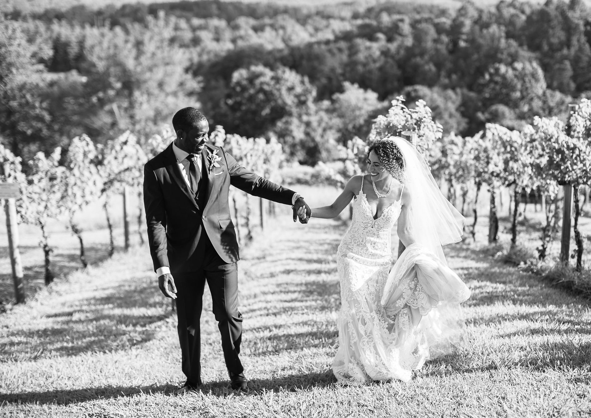 bride and groom holding hands and walking through a vineyard 