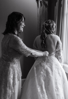 bride's mother helping her put on her dress 