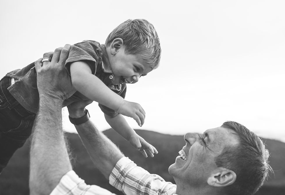 little boy laughing as his dad lifts him in the air
