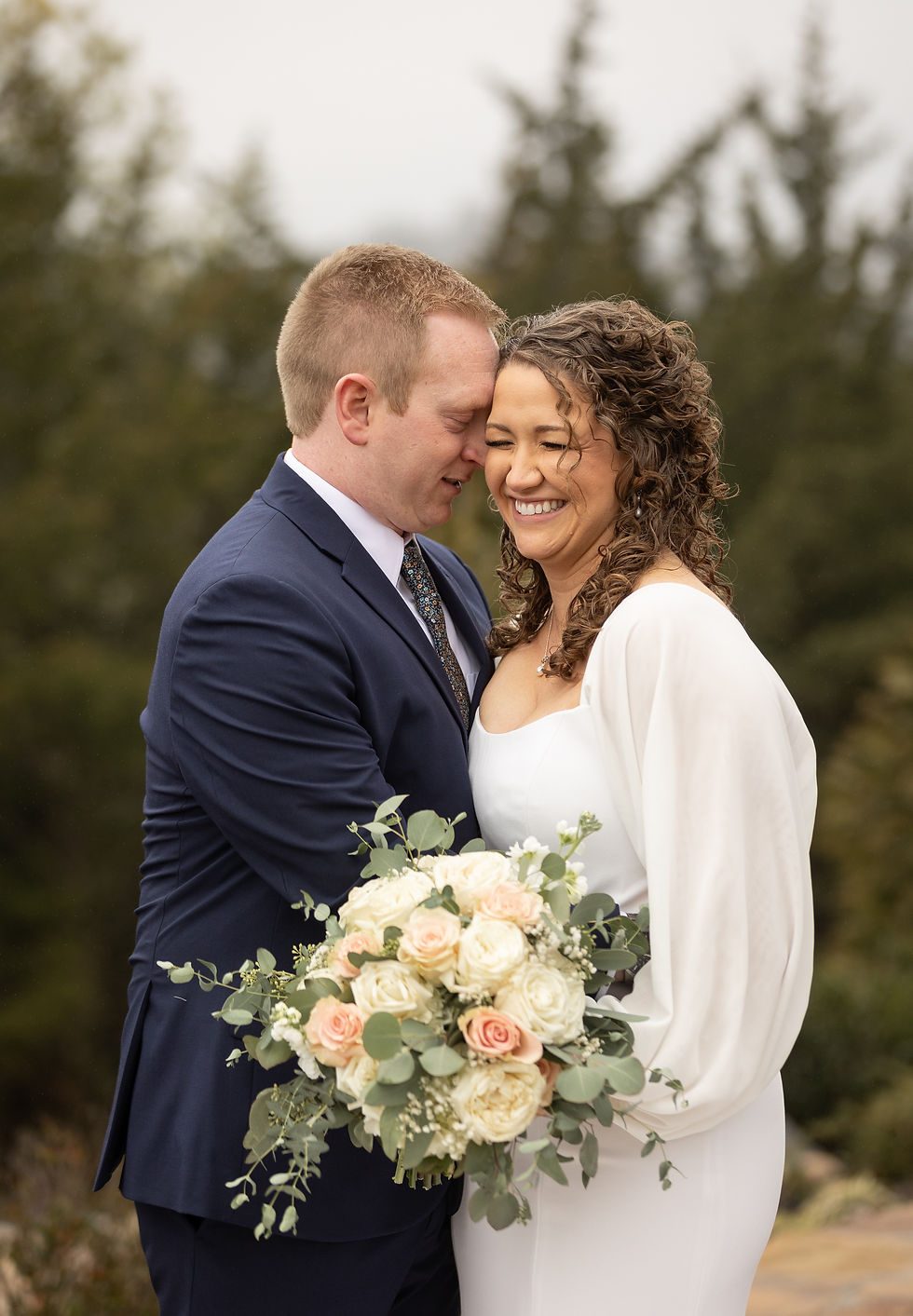 The bride laughing as the groom whispers in her ear.