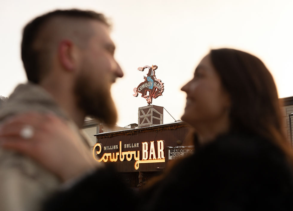 A couple stands facing each other, blurred in the foreground. In the background, a sign reads Million Dollar Cowboy Bar with a cowboy motif.