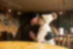 Couple in winter attire shares a kiss in a cozy, wood-paneled cafe with framed photos on the wall, evoking a warm, intimate mood.