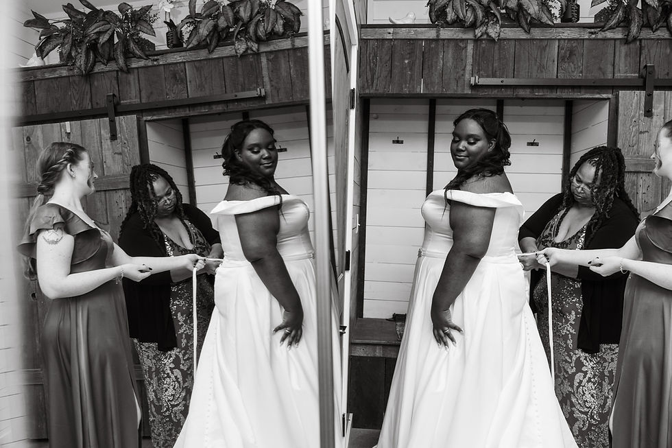 Bride in white gown smiles as two women adjust her dress. Wooden background with plants above creates a cozy atmosphere. Mirror reflection.