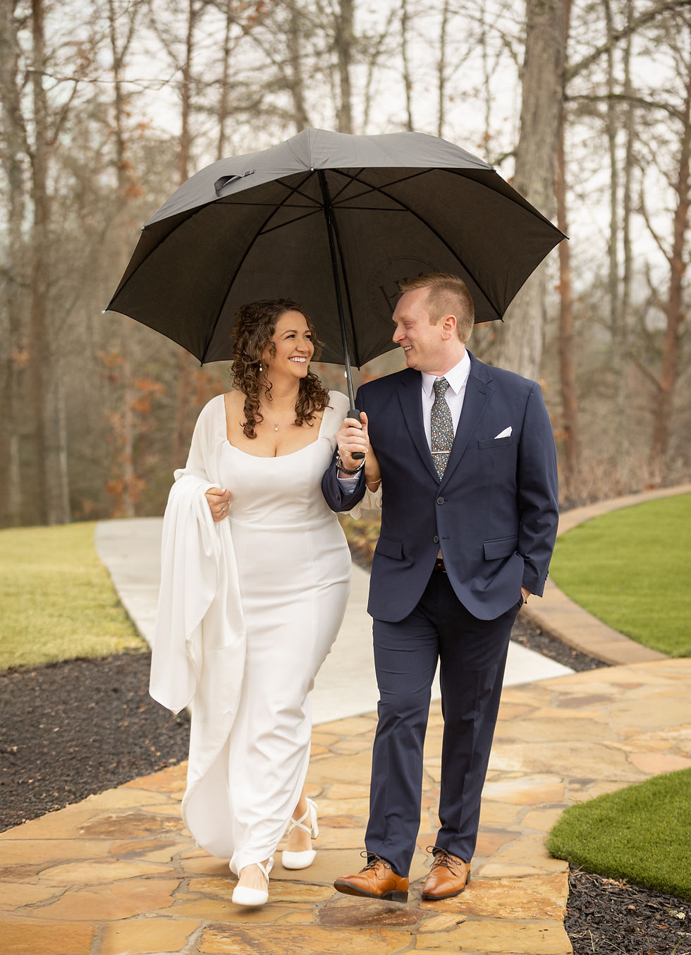 The bride and groom walking together under an umbrella.