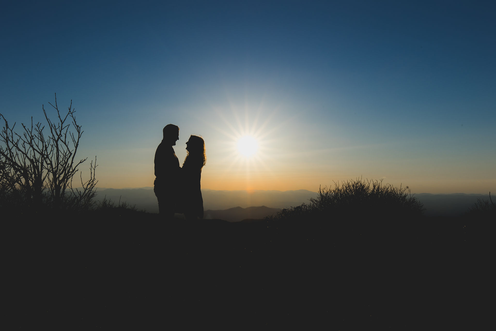 A silhouette of a couple holding each other in front of a blue sky.