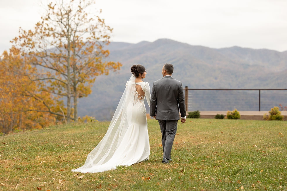 The bride and groom holding hands and walking towards the mountains at the mountain top at The Parker Mill in Whittier, NC.