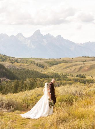 A bride and groom holding hands and walking through a field at The Wedding tree.