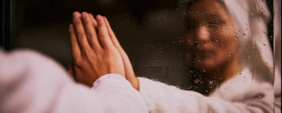 A person pressing their hands against a fogged mirror, with their reflection partially obscured by condensation.
