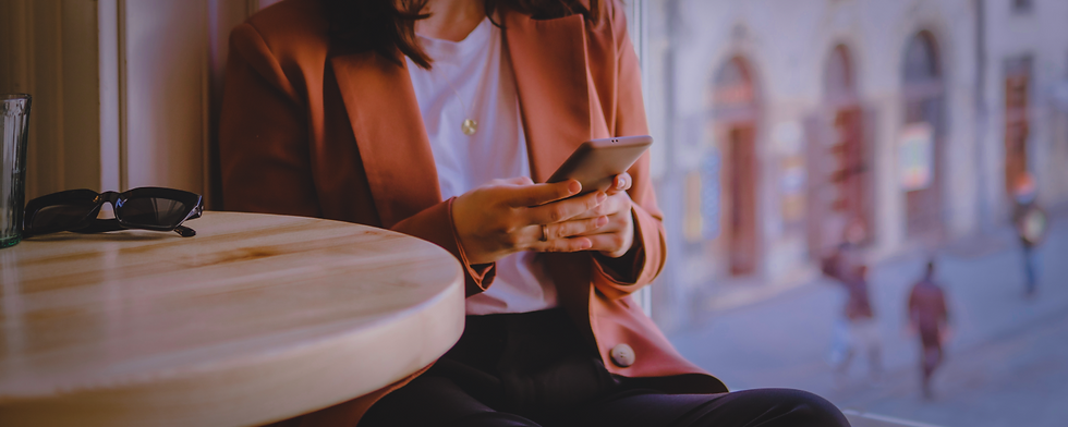 A person seated at a café table by a window, looking down at a smartphone while sitting alone indoors.