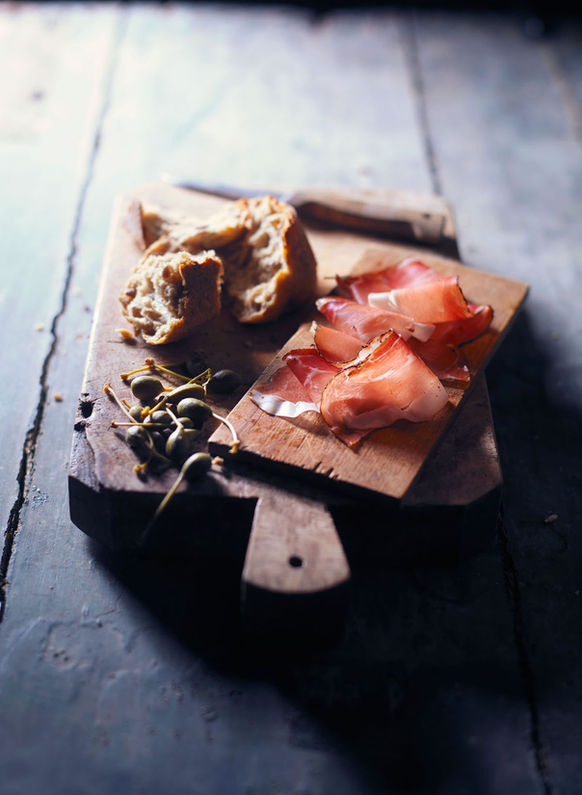 Vleeswaren gepresenteerd op een snijplank, samen met brood, als stilleven gefotografeerd in strijklicht. Charcuterie photography, cured meats