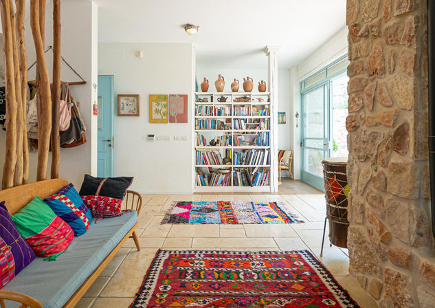 סלון כניסה צבעוני עם ספה, שטיחים, ספרים וקישוטים, עיצוב פנים נעים.