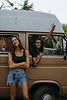two smiling women, one standing against a van, the other in the window of the van.