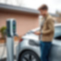 a young man standing next to its electric car and EV charger and charging his car.jpg