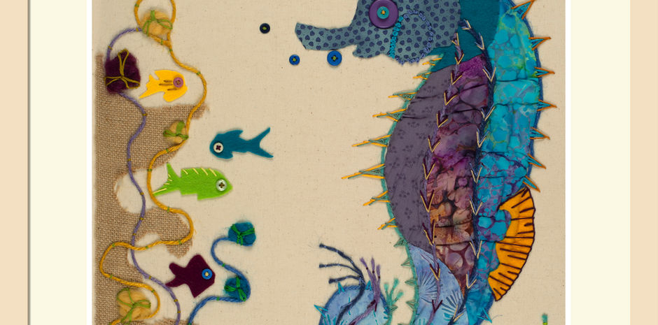 Vibrant fabric artwork of a seahorse in shades of blue with applique textures and embroidery stitches. Surrounded by small fish and swirling patterns, conveying whimsy and creativity.