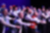 Chorus members performing in a holiday show with their hands reaching forward.