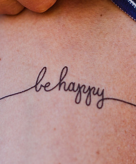 A woman's back with a tattoo that reads, be happy
