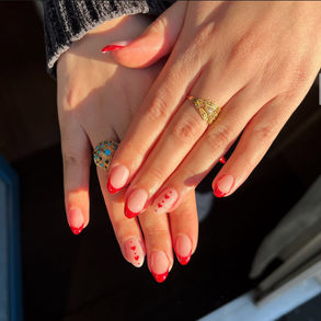 Designet har klassiske røde franske tips, hvor neglespidserne er malet i en smuk, dyb rød farve. På ringefingeren er små delikate hjerter tilføjet som et romantisk touch. Røde Franske Tips med Hjerter på Ringefingeren