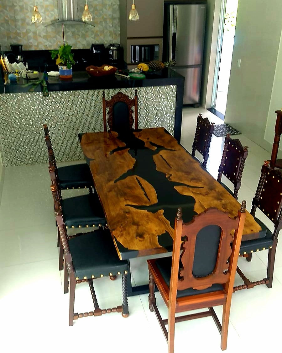 Mesa de jantar de madeira escura com rio de resina preta no meio, cozinha ao fundo